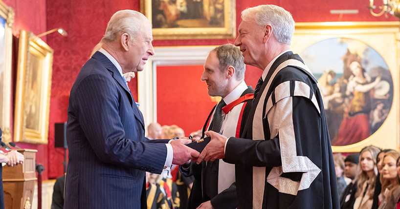 The King in a blue suit shakes hands with the Vice-Chancellor Professor Chris Day who is wearing a full ceremonial black and gold robe. The King in a blue suit shakes hands with the Vice-Chancellor Professor Chris Day who is wearing a full ceremonial black and gold robe.